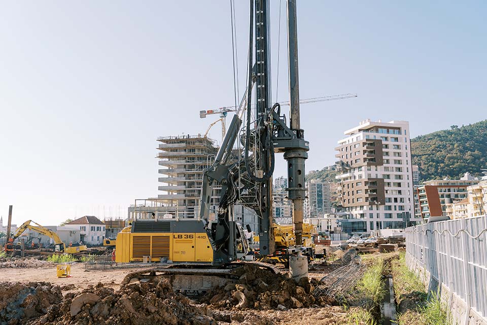 Crawler drilling machine drills the ground to install piles near a multi-storey building